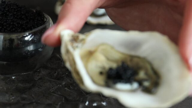 Woman putting tasty black caviar into oyster shell with spoon at textured table, closeup