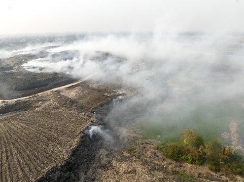 Aminbazar, Bangladesh - 21 February 2026: Aerial view of the Aminbazar landfill with thick white smoke rising from mounds of burning waste and garbage under a hazy sky.
