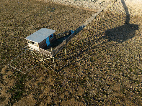 Yves, France - 22 September 2023: Aerial view of a traditional wooden fishing hut on stilts with a long walkway over the rocky tidal flats during low tide.