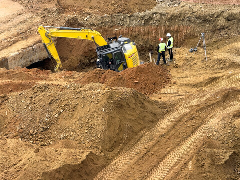 View of a yellow excavator digging in a construction site with two workers standing nearby on brown earth in Avcilar, Istanbul, Turkiye.
