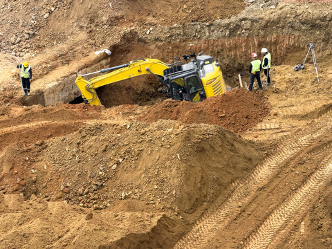 View of a yellow excavator digging in a construction site with workers in safety vests and hard hats on mounds of brown earth Avcilar, Istanbul, Turkiye.