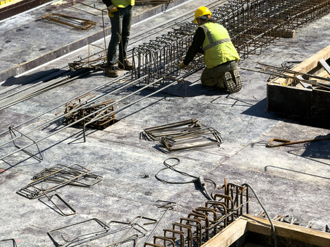 View of construction workers in yellow safety vests and hard hats installing steel rebar cages on a concrete foundation at a building site in Avcilar, Istanbul, Turkey.