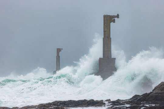View of two concrete lighthouse towers being hit by powerful crashing waves during a storm in the sea off Ushant, Brittany, France.
