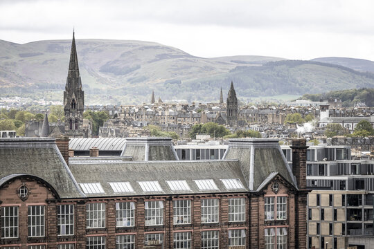 View of historic rooftops and church spires with the rolling hills in the background under an overcast sky in Edinburgh, Scotland, United Kingdom.