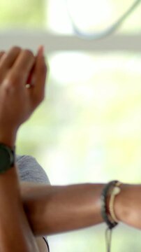 Vertical video: Making finger moves causing arms reaching at window with watch, bracelets, gray top