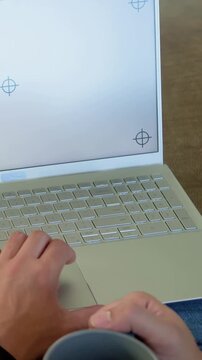 Vertical video: Moving person's left hand tapping keyboard on lap, holding mug, crosshairs, jeans