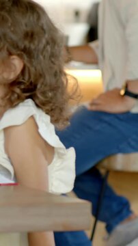 Vertical video: Camera panning toddler wearing white top turning book page at table, copy space