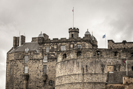 View of the historic stone battlements and towers of Edinburgh Castle under a cloudy sky in Edinburgh, Scotland, United Kingdom.