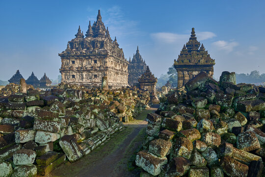 View of the ancient Plaosan Lor Temple complex featuring intricate stone carvings and scattered ruins under a clear blue sky in Prambanan, Special Region of Yogyakarta, Indonesia.