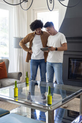 Obraz premium Diverse male friends leaning in, examining tablet while standing in living room with green bottles