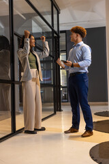Fototapeta premium Diverse coworkers cheering success via glass divider at office wearing office wear with smartphone