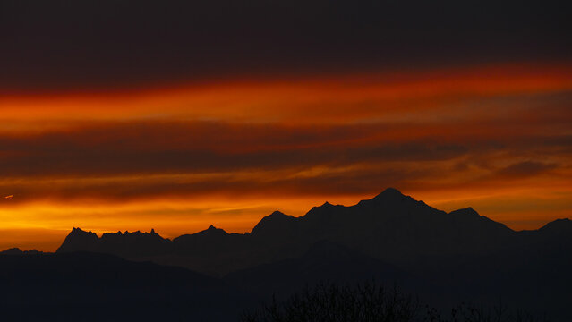 View of the silhouette of the Mont Blanc massif under a dramatic sunset sky with orange and dark clouds in Chamonix, Auvergne-Rhone-Alpes, France.