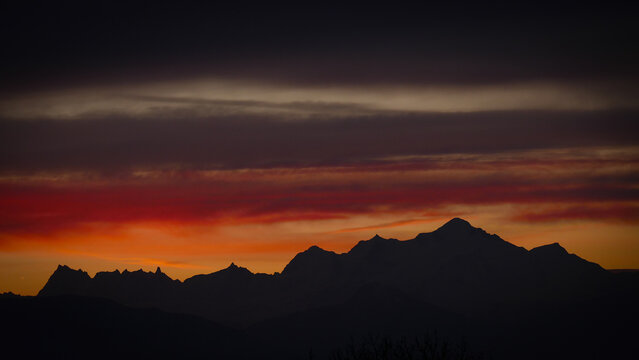 View of the silhouette of the Mont Blanc massif under a dramatic sunset sky with vibrant orange and red clouds in Chamonix, Auvergne-Rhone-Alpes, France.