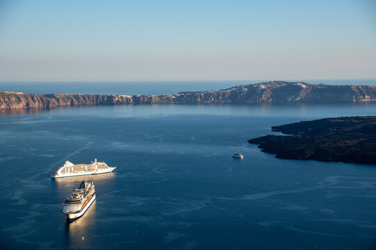 View of cruise ships anchored in the blue waters of the Santorini caldera under a clear sky in Fira, Greece.