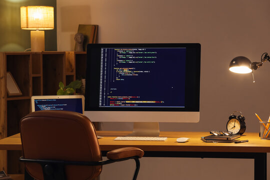 Programmer's workplace with computer and glowing lamp in dark office
