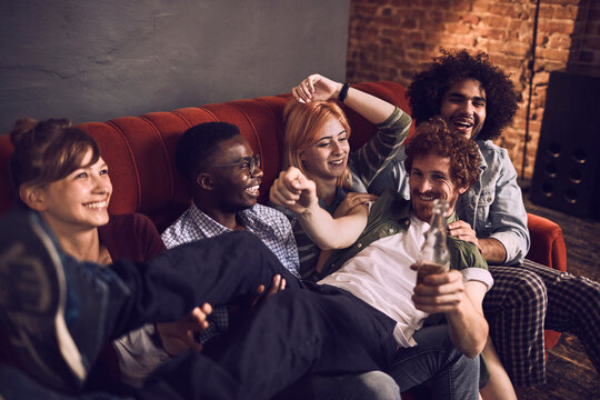 Young friends laughing together on sofa at cozy loft party
