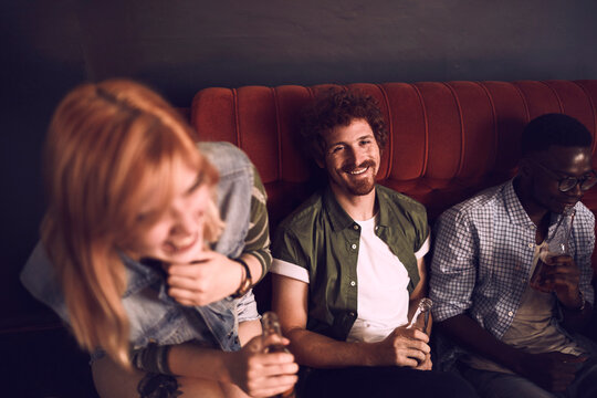 Young friends laughing and drinking in cozy bar booth
