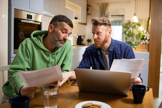 Two men reviewing household bills on laptop at home kitchen