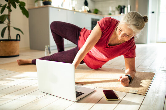 Senior woman doing side plank during online home workout
