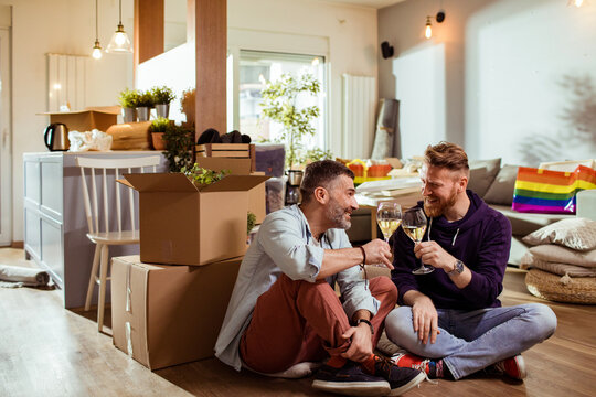 Two men toasting wine in new apartment with moving boxes