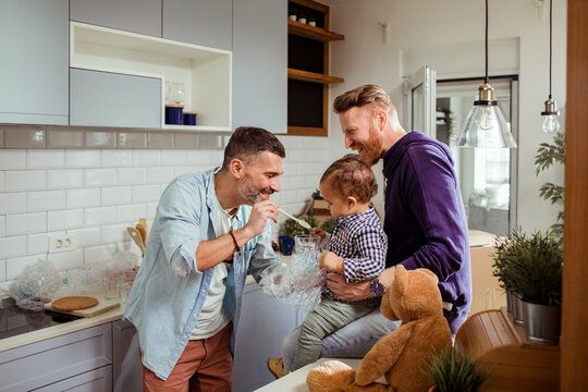 Two men playing with toddler in modern kitchen