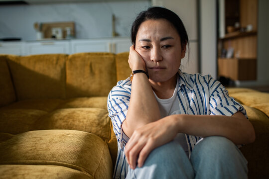 Sad woman sitting on living room floor at home