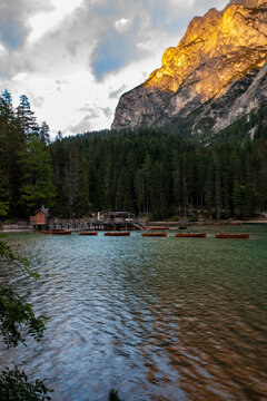 View of Pragser Wildsee with wooden rowing boats on the water, a wooden boathouse, and a mountain peak glowing in golden light Prags, Trentino-Alto Adige, Italy.