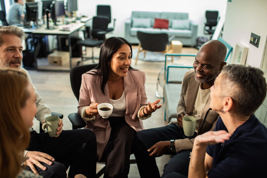 Diverse coworkers chatting during coffee break in modern office lounge