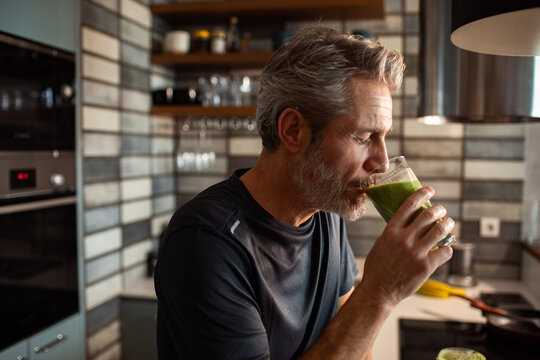 Middle-aged man drinking green smoothie in modern kitchen