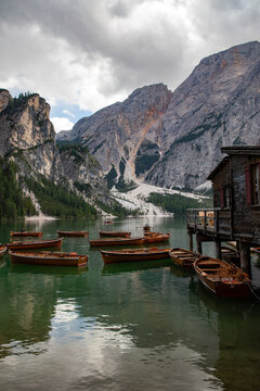 View of wooden rowing boats on the emerald waters of Pragser Wildsee with a rustic boathouse and the towering Seekofel mountain under a cloudy sky Prags, Trentino-Alto Adige, Italy.
