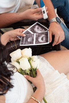 Happy couple holding a positive pregnancy test and ultrasound scans with a bouquet of white roses.