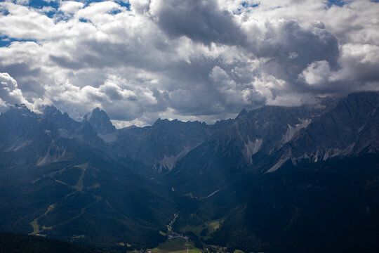 View of the jagged peaks of the Dolomites under a dramatic cloudy sky with deep valleys and dense evergreen forests in the Italian Alps Rocca Pietore, Veneto, Italy.