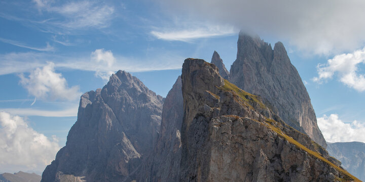 View of the jagged peaks of the Mt Seceda Dolomites with rocky slopes and wispy clouds under a blue sky in Rocca Pietore, Veneto, Italy.