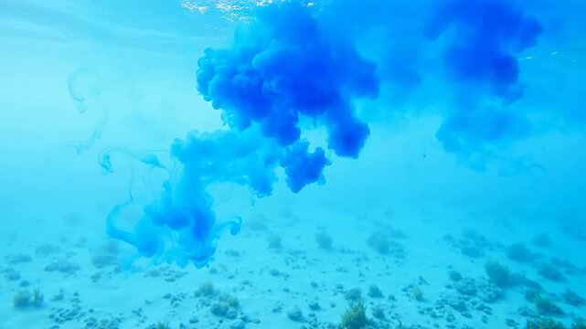 Abstract underwater blue ink cloud diffusion in clear turquoise water with sandy seabed