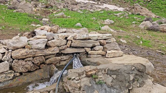 Crystal clear spring water gushes through stacked stones into a stone trough in a remote wild alpine meadow with melting snow and rugged peaks.
📍 Hawraman Takht, Kurdistan, Iran 