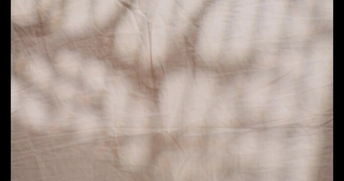 The play of natural shadows from leaves or windows moving gently. Warm afternoon sunlight casts abstract patterns on the surface of creased cotton or linen in creamy beige.