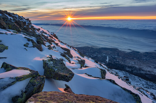 View of the snowy slopes of Slavkovsky stit at sunrise with a sun starburst over a sea of clouds Vysoke Tatry, Presovsky kraj, Slovakia.