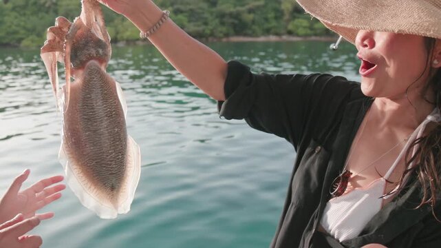 A woman in a straw hat shows off a freshly caught cuttlefish while on a boat trip in the clear waters of Koh Kood, Thailand