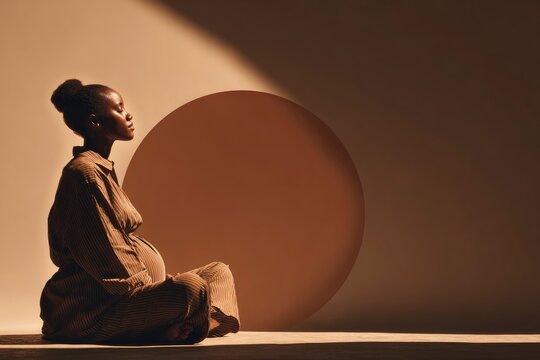 Pregnant african woman sitting in meditation with circular lighting in a moody studio shot for maternity wellness marketing