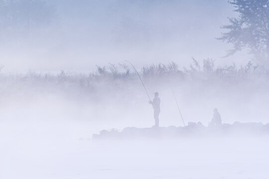 View of fishermen standing on a rocky bank with fishing rods in thick morning fog and mist Wisla, Silesian Voivodeship, Poland.