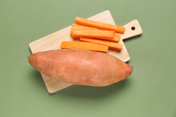 Cutting board and fresh sweet potato on green background