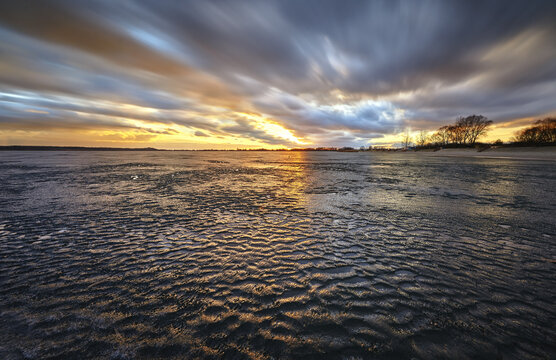 View of the frozen surface of Lake Tarnobrzeg with rippled ice under a dramatic sunset sky with moving clouds Tarnobrzeg, Podkarpackie, Poland.