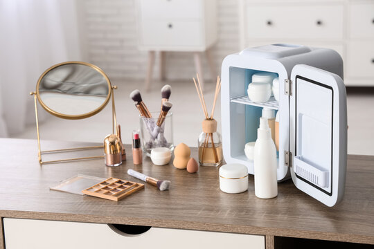 Small cosmetic refrigerator, diffuser and mirror on table near white wall. Closeup