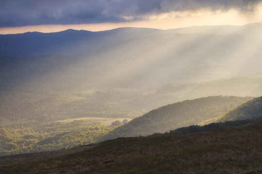 View of sunbeams breaking through clouds over the forested peaks and valleys of the Bieszczady Mountains during sunset Bieszczady County, Podkarpackie Voivodeship, Poland.