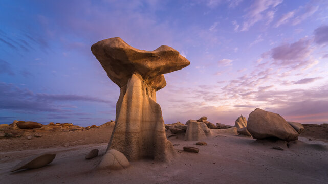 View of a mushroom-shaped hoodoo rock formation in the Bisti Badlands under a purple sunset sky in San Juan County, New Mexico, United States.