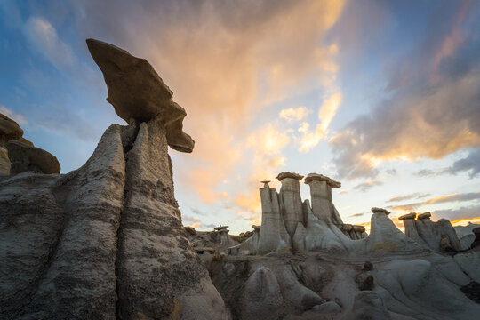 View of the unique hoodoo rock formations of the Bisti Badlands under a dramatic sunset sky with golden clouds San Juan County, New Mexico, United States.