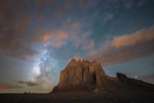 View of the majestic Shiprock rock formation under a starry night sky with the Milky Way and glowing clouds Shiprock, New Mexico, United States.