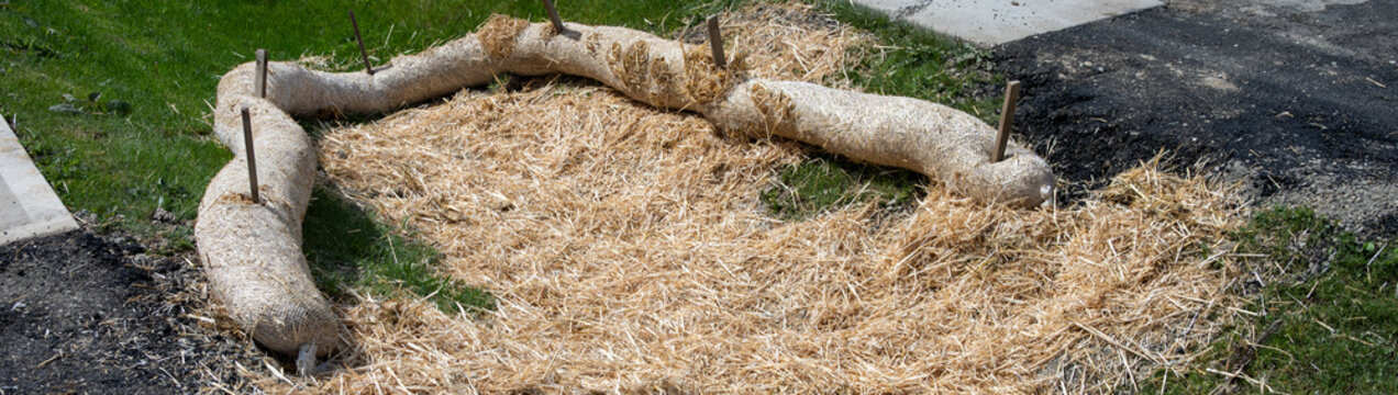 Straw wattle in stormwater drainage ditch, and straw scattered over grass, to filter out construction debris, concrete sidewalk and asphalt road
