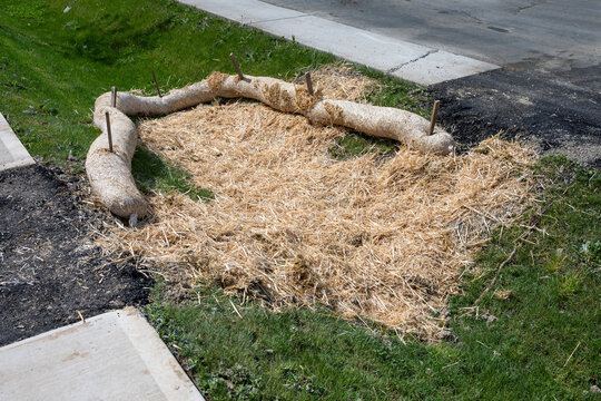 Straw wattle in stormwater drainage ditch, and straw scattered over grass, to filter out construction debris, concrete sidewalk and asphalt road
