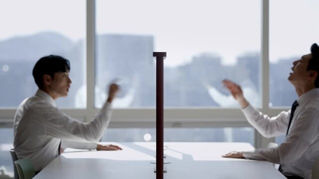 Two businessmen pointing across a table with a divider, symbolizing communication challenges, negotiation, or competition in a modern office setting.